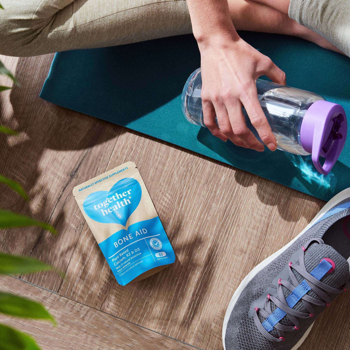 Together Health Bone Aid Nahrungsergänzungsmittel neben einer Wasserflasche und Yoga-Matte.