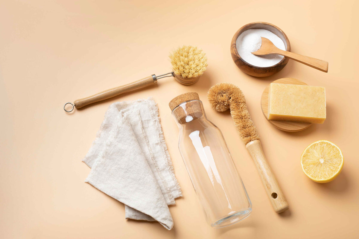 Nachhaltige Haushaltsprodukte mit Glasflasche, Naturseife, Holzbürsten und Leinentuch.