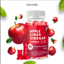 Eine Flasche Harmonify Apfelessig-Gummibärchen, umgeben von fallenden Äpfeln und Blättern, weist auf die natürliche Apfelbasis des Produkts hin.