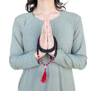 Eine Person, die ihre Hände in einer Gebetshaltung (Anjali Mudra) zusammenhält, wobei eine schwarz-rosa Mala-Gebetskette um ihre Handgelenke gewickelt ist.