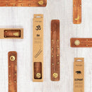 Verschiedene Weihrauchhalter aus Holz mit goldenen Symbolen und deren Kartonverpackung.