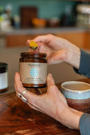 Eine Person hält ein Glas Paavani Ayurveda Pitta Spice Blend und einen kleinen Löffel, der mit gelbem Pulver gefüllt ist.