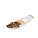 Getrocknete Kräutermischung mit Rosenblättern, die aus einer geöffneten braunen Papiertüte herausfällt.