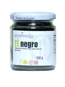 Glasgefäß mit losem schwarzem Tee, weißem Etikett und silbernem Deckel. Auf dem Etikett steht "ayurveda TE negro" und "100 g", mit Symbolen für 100% Natur, glutenfrei und ohne GVO.