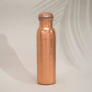 Eine hohe, glänzende Kupferwasserflasche mit einem detaillierten, gravierten floralen oder Paisley-Muster, unter sanftem Licht.