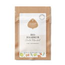 Eine braune Tüte mit weißem Etikett, Produktname „Bio Haarkur Amla Mandel“, illustriert mit Mandeln und Amla-Früchten.