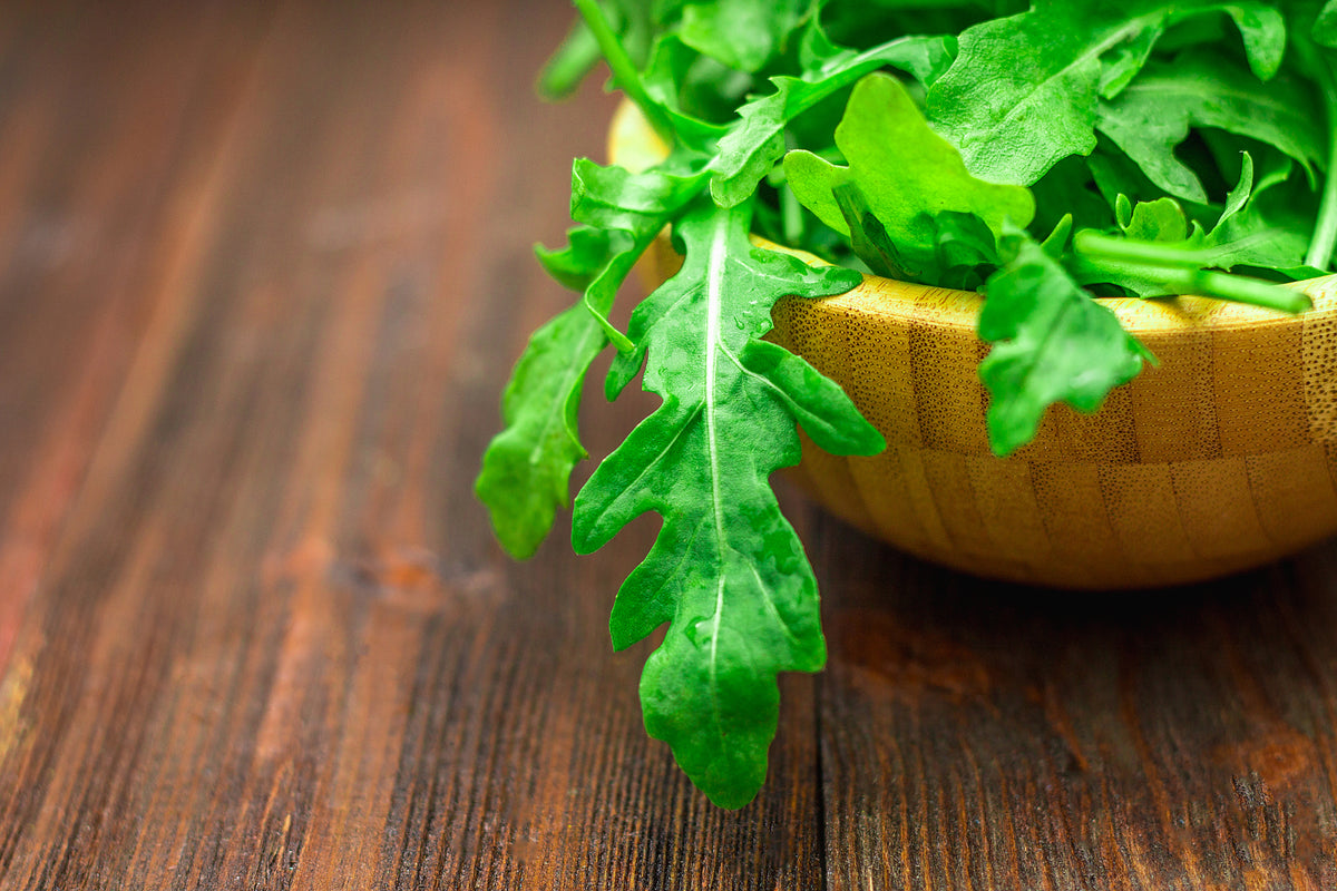 Frischer grüner Rucola in einer Holzschale auf einem dunklen Holztisch.