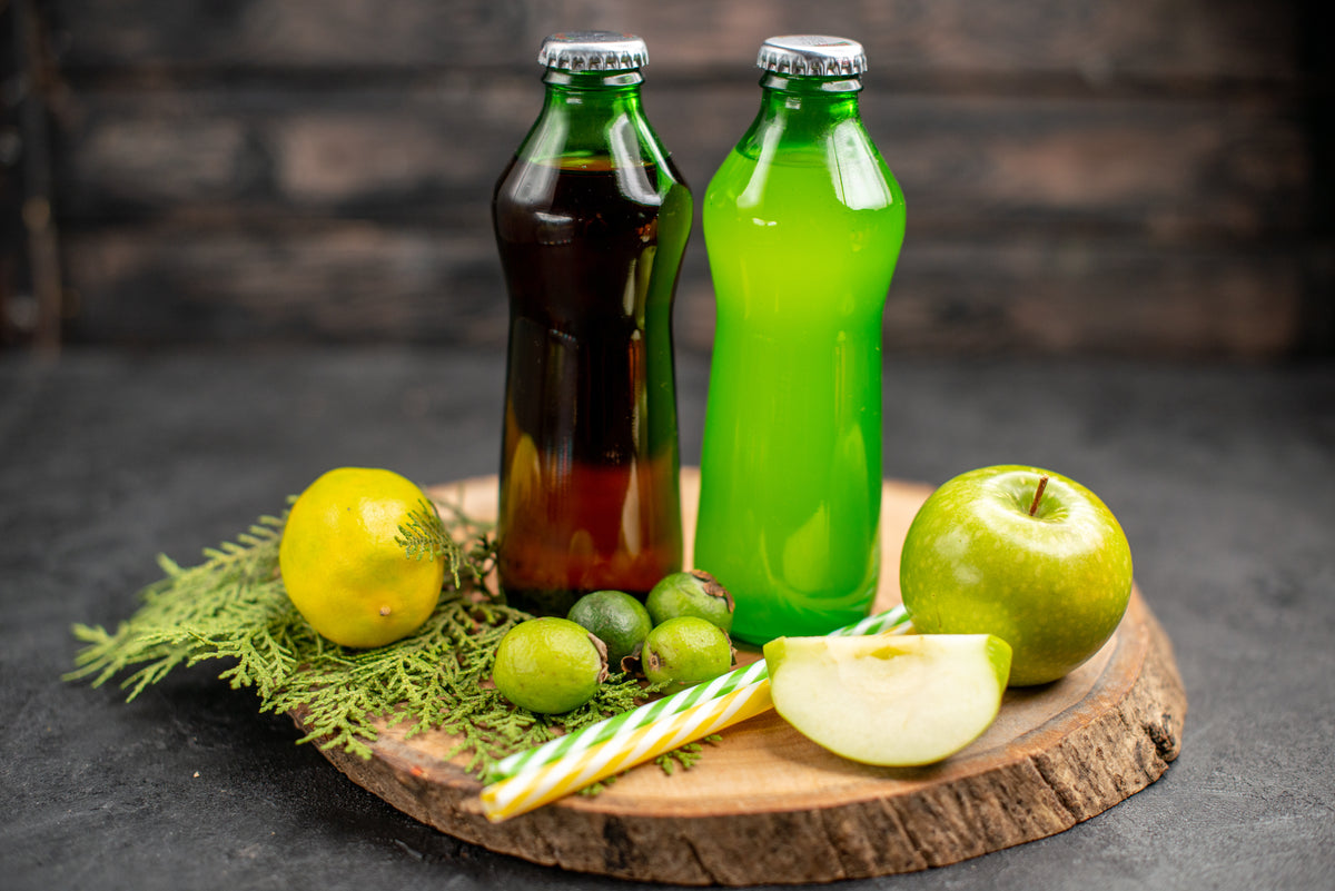 Zwei Flaschen Bio-Saft mit grünem und dunklem Fruchtsaft auf einem Holzbrett mit Äpfeln.