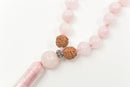 Nahaufnahme einer Mala-Gebetskette aus hellrosa Rosenquarz-Kugeln mit zwei Rudraksha-Samen und einer Quaste.