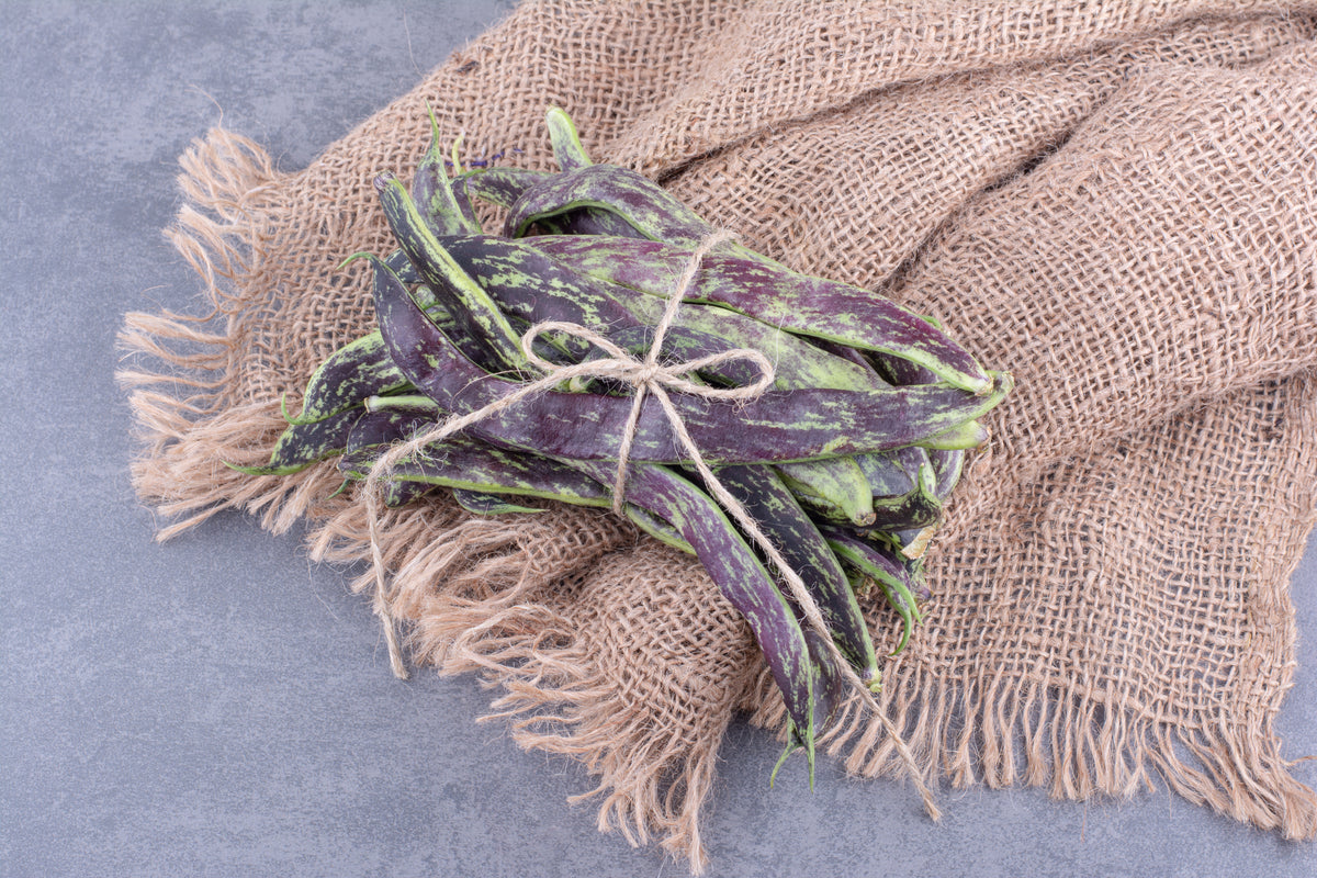 Frische violette Bohnen auf grobem Sackleinen, Bio-Gemüse für gesunde Ernährung.