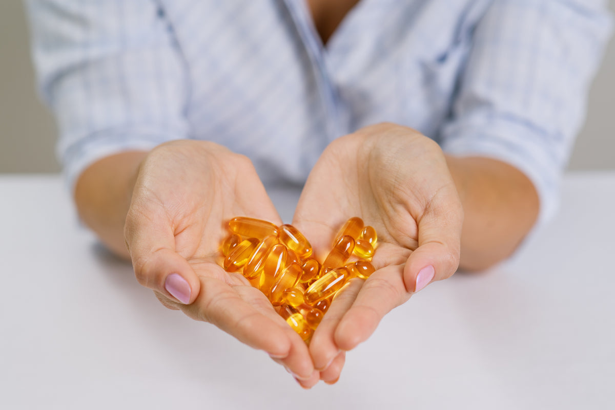 Zwei Hände halten goldene Omega-3 Kapseln in Herzform für gesunde Ernährung.
