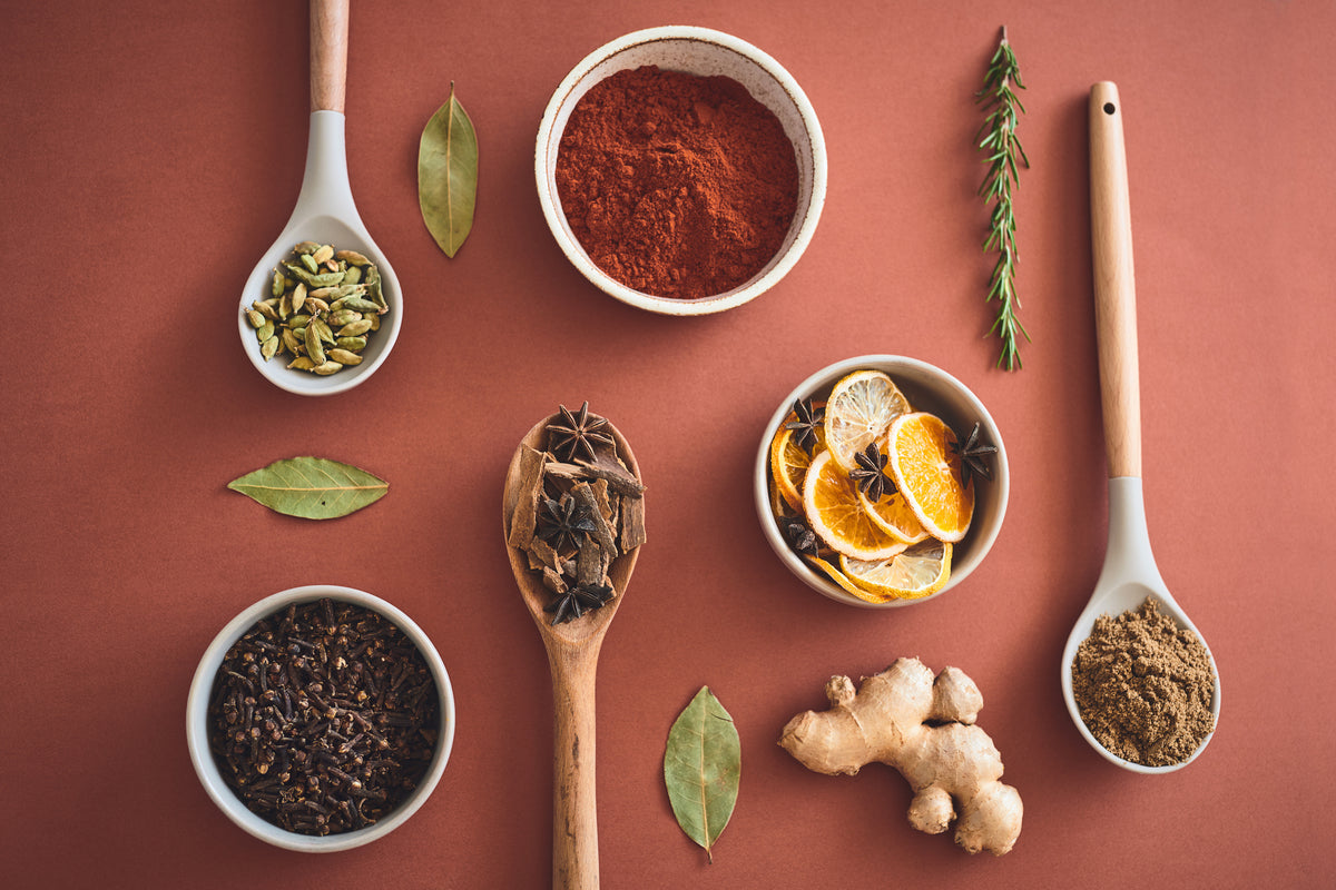 Vielfältige Bio-Gewürze wie Paprika, Ingwer, Sternanis und Kräuter auf rötlichem Hintergrund.