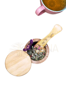 Ein holz-mörser mit pestle gefüllt mit getrockneten kräutern und blumen in natürlicher hellholzoptik für heart chakra anahata grüntee von ayamani naturals