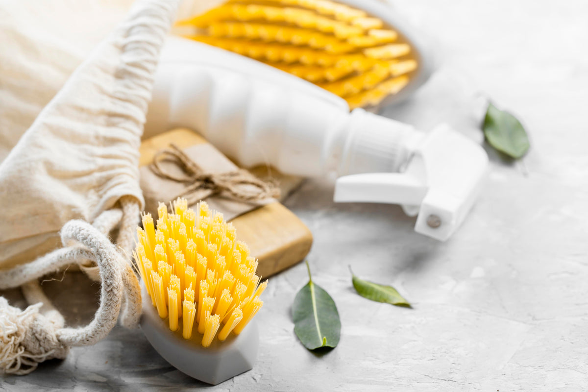 Nachhaltige Reinigungsmittel: Sprühflasche, Naturseife und Spülbürste auf hellem Untergrund.