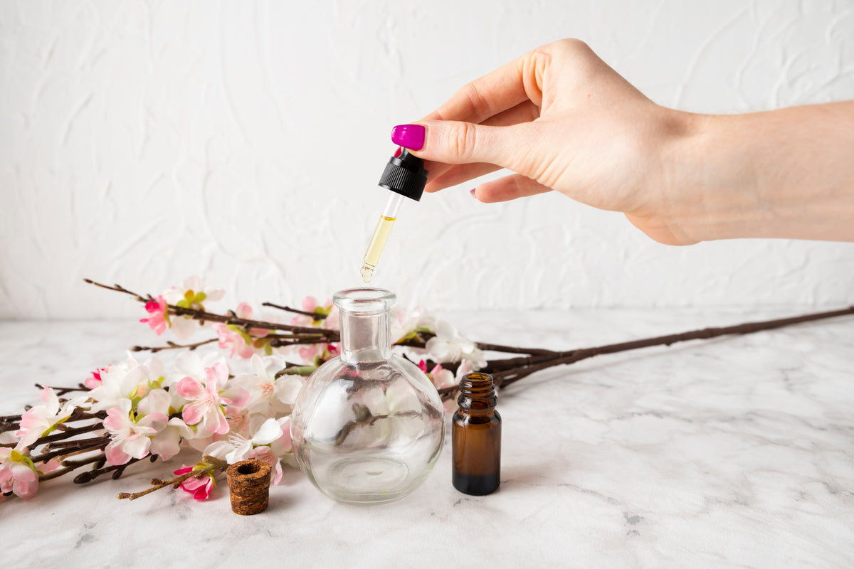 Hand mit Pipette tropft ätherisches Öl in eine Glasflasche neben Kirschblüten.