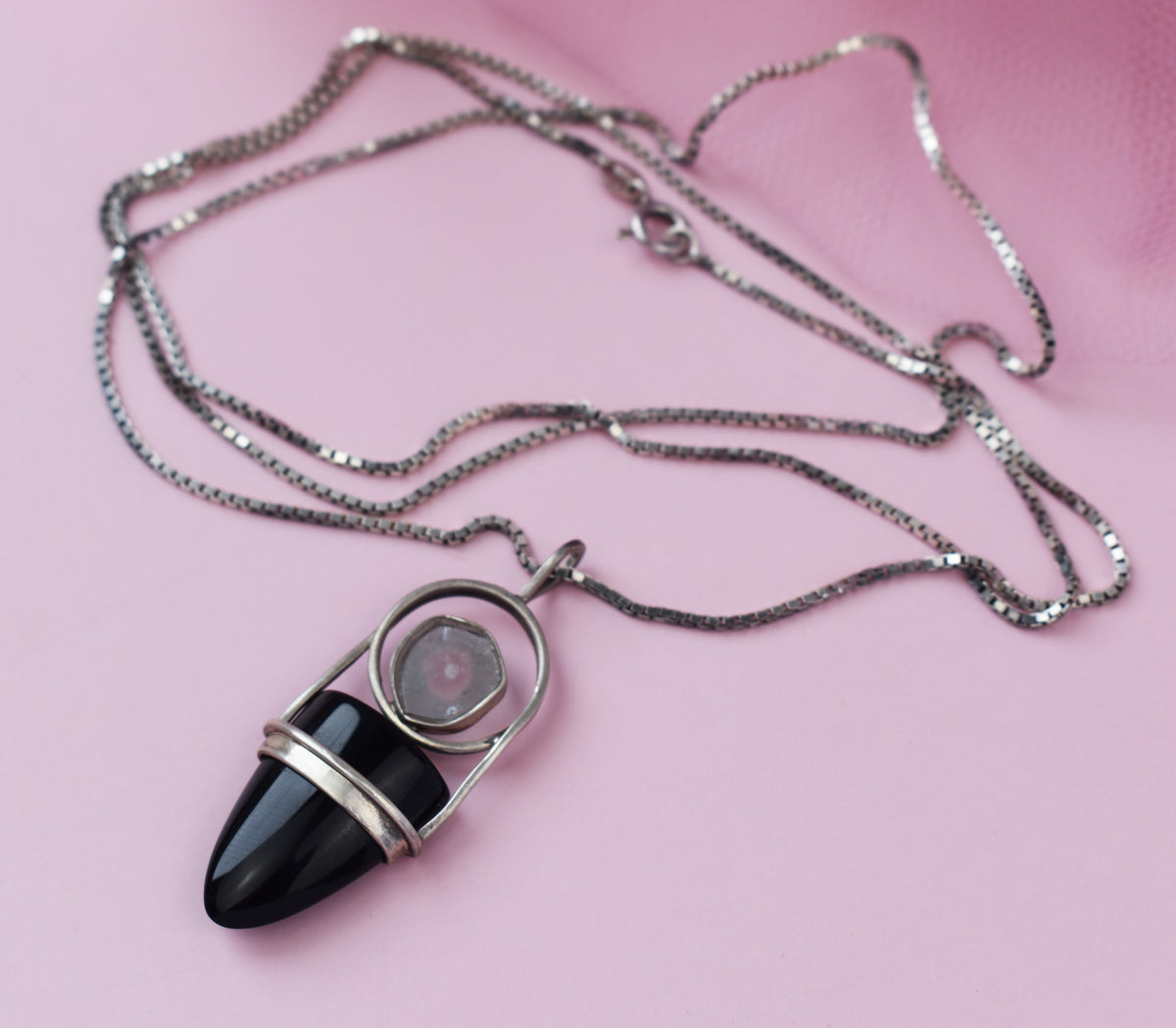 Silberne Halskette mit schwarzem Onyx-Anhänger auf rosa Hintergrund