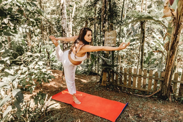 Eine Frau macht eine Yogaposition auf einer roten Matte in einem Wald.