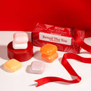 Verschiedene bunte runde Seifenstücke, präsentiert neben einer roten Koji White Geschenkbox und einem Seidenband.