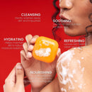 Eine Person hält ein orangefarbenes Stück Seife vor einem roten Hintergrund mit Text über die Vorteile.