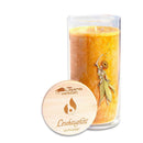 Eine hohe gelbe Kerze in einem mit Blumenmuster verzierten Glashalter, neben einem runden Holzdeckel mit der Aufschrift „Leichtigkeit“.