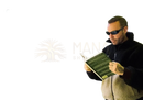 Ein mann mit sonnenbrille und schwarz-beiger fleecejacke liest ein buch mit grünen seiten vor grauer holzwand für klare sicht