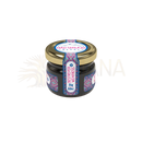 Ein kleiner dunkler glasbehälter mit goldenem deckel und dekorativem blau-rosa-weißem etikett mad shilajit nepal shilajit resin