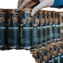 Schwarze zylindrische dose maitake pilzflüssigkeit von feelsupreme mit braunem pilzmotiv und grünem schriftzug