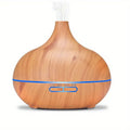 Ein tropfenförmiger Aroma-Diffuser für ätherische Öle in heller Holzoptik, mit einem dünnen blauen LED-Leuchtstreifen und sichtbarem Nebel, der oben austritt.