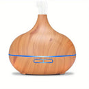 Ein tropfenförmiger Aroma-Diffuser für ätherische Öle in heller Holzoptik, mit einem dünnen blauen LED-Leuchtstreifen und sichtbarem Nebel, der oben austritt.