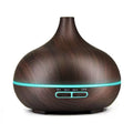 Ein tropfenförmiger Ultraschall-Aroma-Diffuser in dunkelbrauner Holzoptik mit einem dünnen türkisfarbenen LED-Leuchtring und zwei Bedientasten.