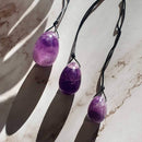 Amethyst Yoni Eierpackung mit Loch und Schnur, Schmuck von Mana Kendra, aus violettem Amethyst mit Schnur und Loch.