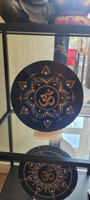 Eine schwarze Vinyl-Schallplatte mit einem gold-blauen Punktmalerei-Mandala und einem zentralen goldenen Om-Symbol, präsentiert auf einem Glasregal.