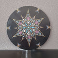 Eine schwarze Vinyl-Schallplatte mit einem lebendigen Punktmalerei-Mandala eines bunten Baumes, präsentiert auf einem Holzständer vor weißem Hintergrund.