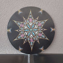 Eine schwarze Vinyl-Schallplatte mit einem lebendigen Punktmalerei-Mandala eines bunten Baumes, präsentiert auf einem Holzständer vor weißem Hintergrund.