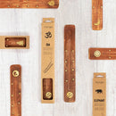 Verschiedene Weihrauchhalter aus Holz mit goldenen Symbolen und deren Kartonverpackung.