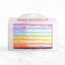 Eine weiße Chakra Balancing Kit Box von Myga, die sieben farbige, gestapelte Päckchen mit Räucherstäbchen enthält, die jeweils einem anderen Chakra zugeordnet sind.