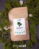 Eine Packung myVial Bio Chlorella Tabletten, präsentiert mit grünem Moos und Muscheln.