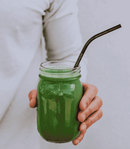 Eine Hand, die ein mit einem grünen Smoothie gefülltes Einmachglas mit einem Metallhalm hält.
