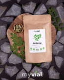 Eine Packung myVial Bio Moringa Kapseln auf einem Holzbrett mit Blättern und Steinen.