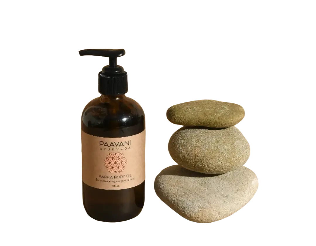 A dunkles bernsteinfarbenes glasfläschchen mit schwarzem pumpenspender und beige etikett von paavani ayurveda kapha körperöl kurma body oil