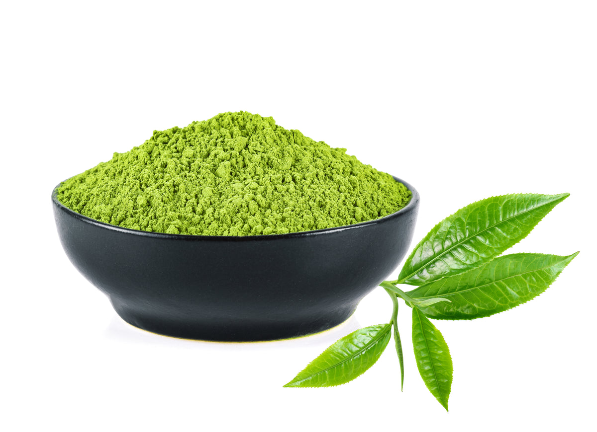 Grünes Matcha-Pulver in einer schwarzen Schale mit frischen Teeblättern auf weißem Hintergrund