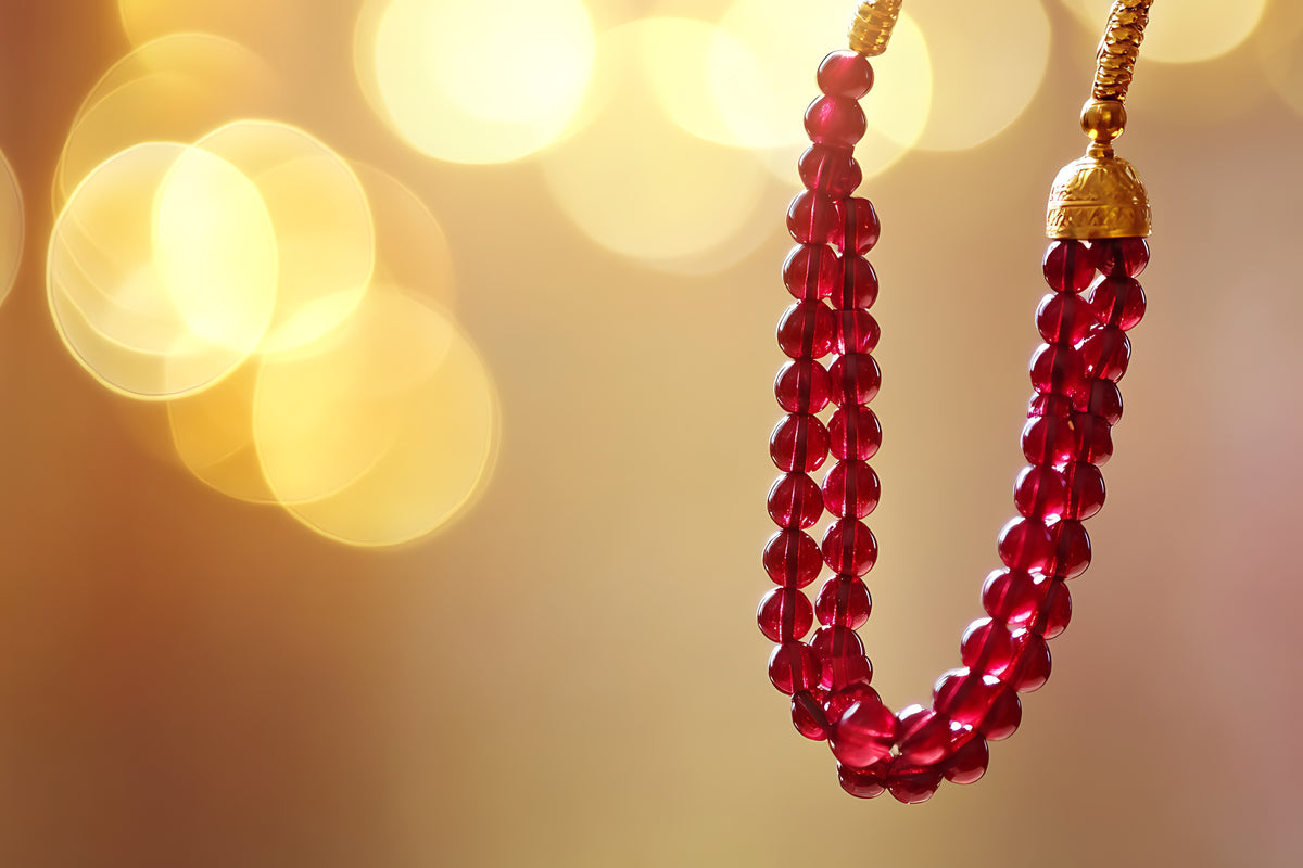 Elegante rote Perlenkette mit goldenen Details vor goldenem Bokeh-Hintergrund.