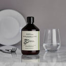 Eine Lifestyle-Aufnahme einer braunen Flasche „Read/the/label“ Spülmittel mit Bergamotte & Grosso-Lavendel auf einer Marmoroberfläche neben einem Glas Wasser und einem weißen Teller.