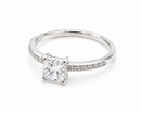 Silberner Verlobungsring mit einem Prinzessschliff-Diamant-Solitär und seitlichen Pavé-Steinen auf weißem Hintergrund.