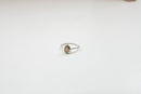 Ein silberner Ring mit gedrehter Ringschiene und einem birnenförmigen, hellbraunen Stein, auf einem weißen Hintergrund.