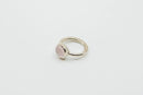  Ein silberner Ring mit einer schlichten, leicht strukturierten Ringschiene und einem kleinen, ovalen, polierten rosa Stein, auf einem weißen Hintergrund.