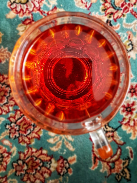 Ein Glas roter Tee von oben gesehen vor einem gemusterten Hintergrund.