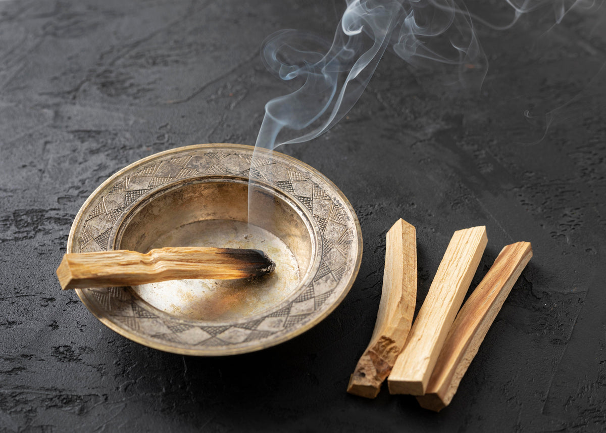 Räucherstäbchen aus reinem Palo Santo in einer verzierten Metallschale mit aufsteigendem Rauch.