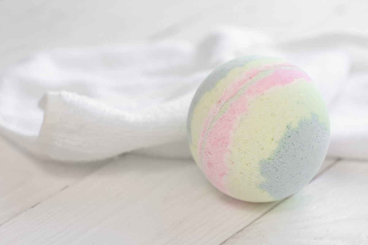 Bunte Badebombe in Pastellfarben auf weißem Holz mit weichem Handtuch