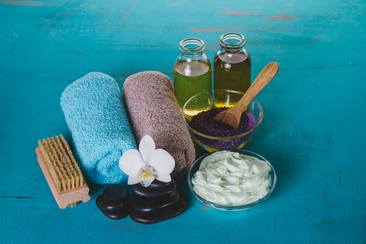 Wellness-Set mit Massageöl, Handtüchern, Körpercreme, Salzkörperpeeling und einer Orchidee.